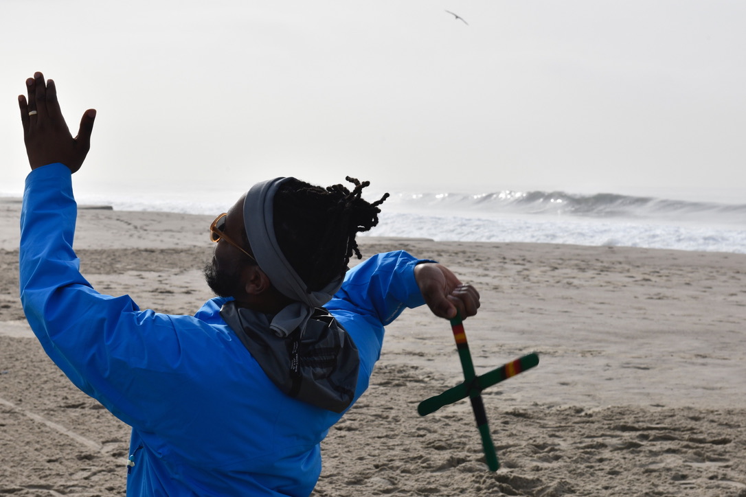 A boomerang thrower on the beach in a blue jacket